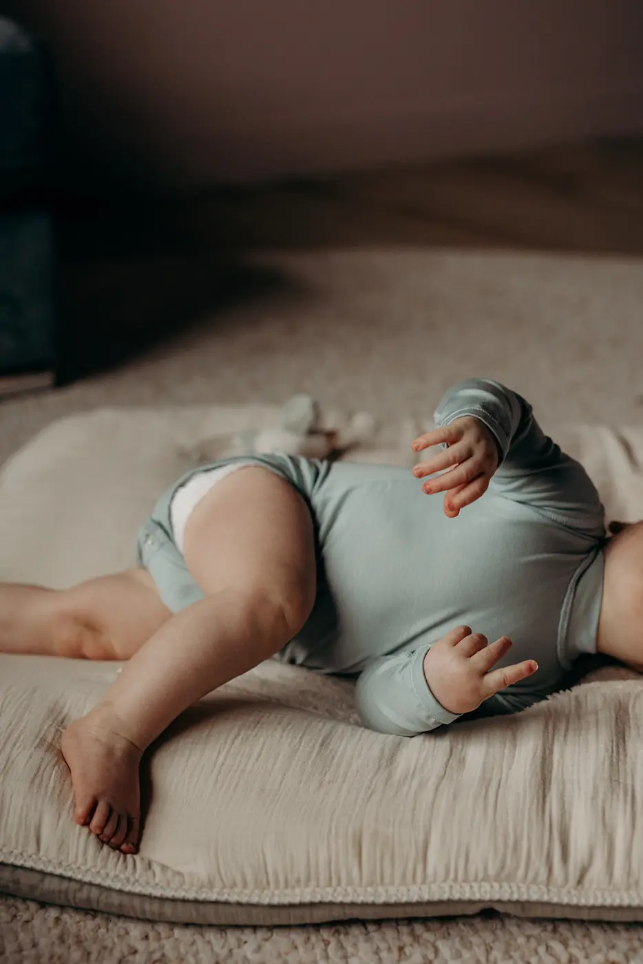 Baby in een mintgroene romper met lange mouwen op een beddensprei