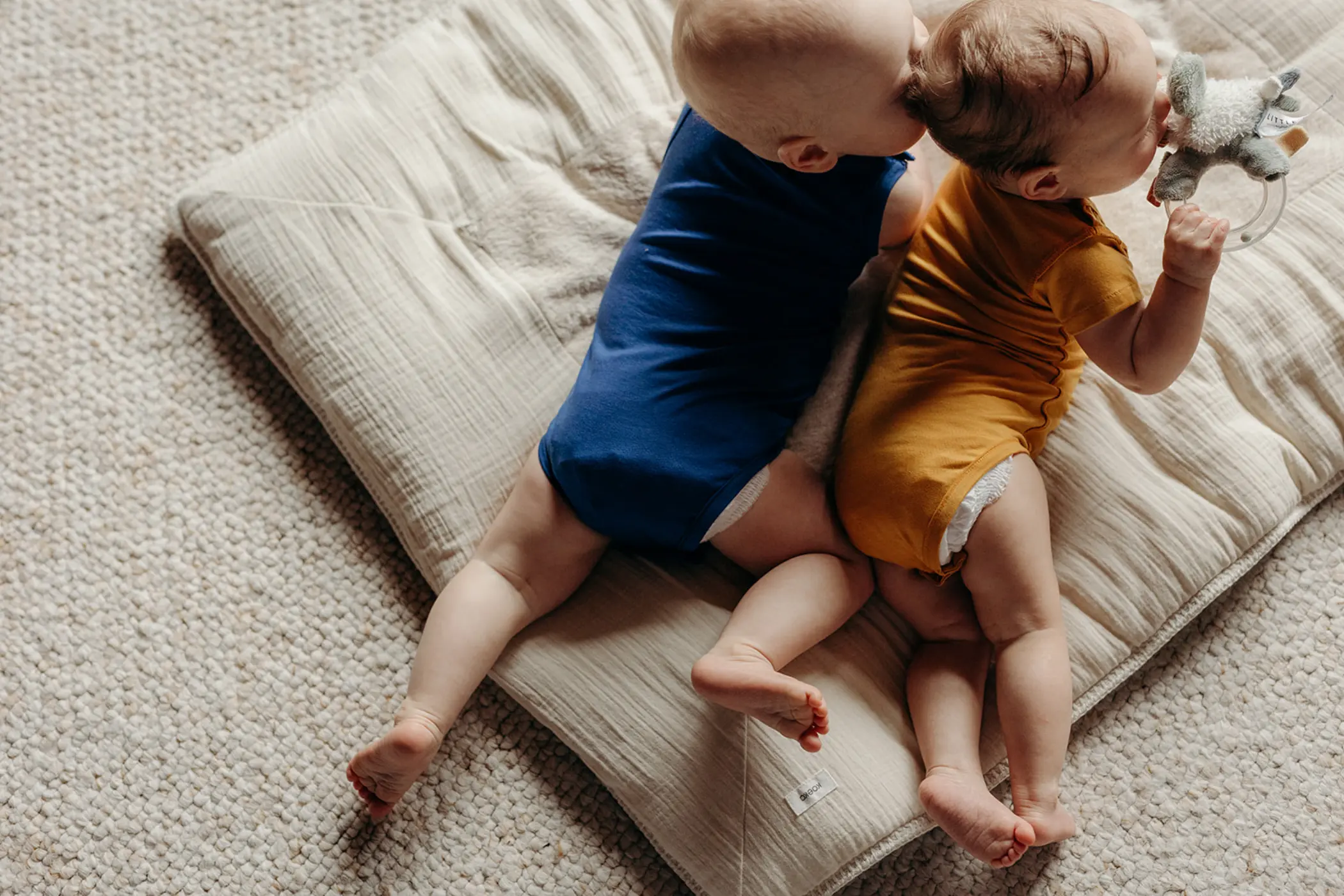 Twee baby's naast elkaar in een donkerblauwe en een okergele romper