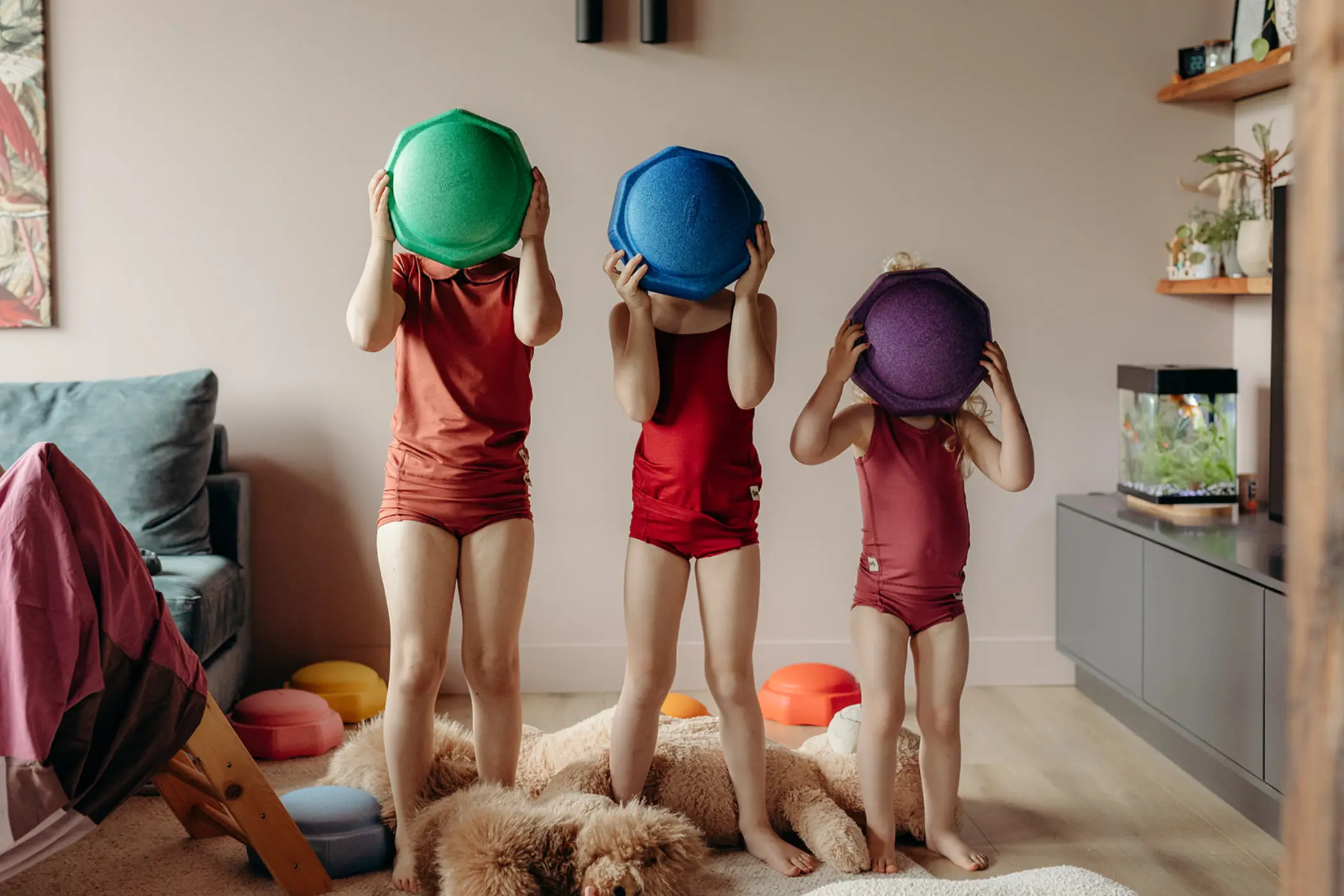 Drie kinderen op een rij in Noorderdon-kleding, elk met een gekleurde speelschijf voor het gezicht