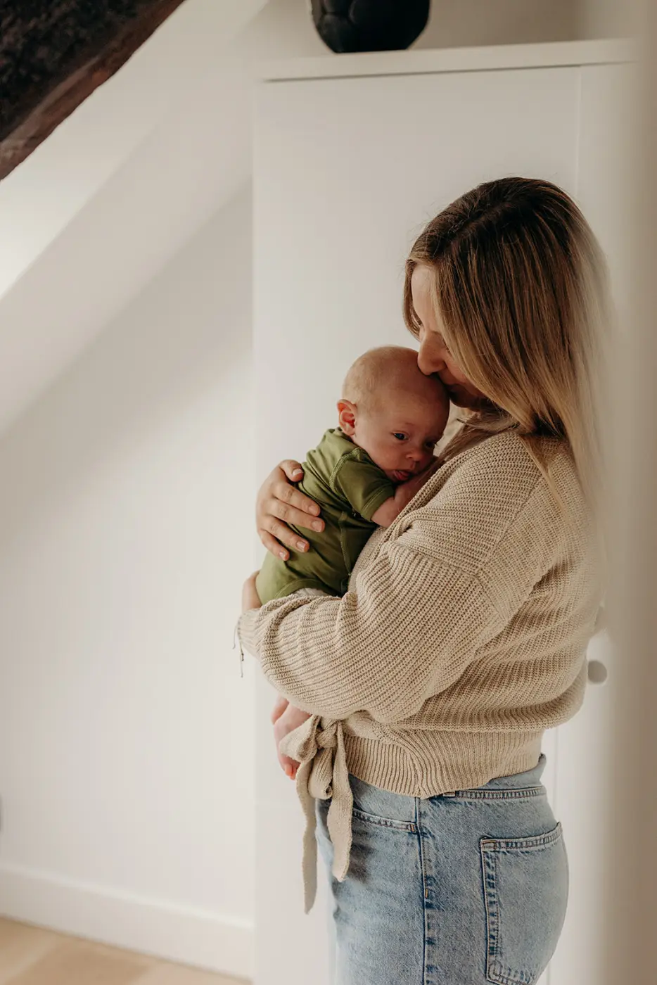 Ouder houdt een pasgeboren baby in een olijfgroene romper tegen zich aan